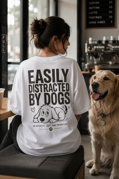 Person wearing a t-shirt with 'Easily Distracted by Dogs' text and a dog sitting next to them in a cafe.